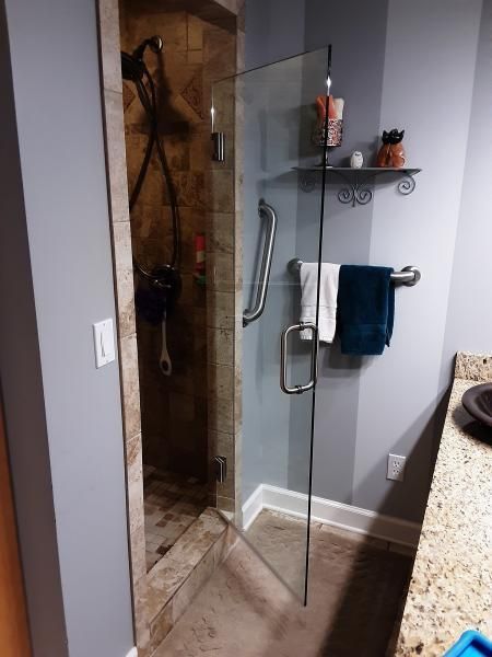 A glass-door shower with a grab bar on the wall and the door, located in a bathroom with a granite-topped vanity.