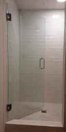 A glass shower door with a silver handle and hinges, installed in a bathroom with white horizontal subway tile walls.