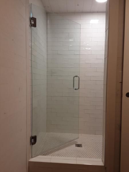 A frameless glass shower door with a handle, hinges, and white subway-tiled walls in a small bathroom.