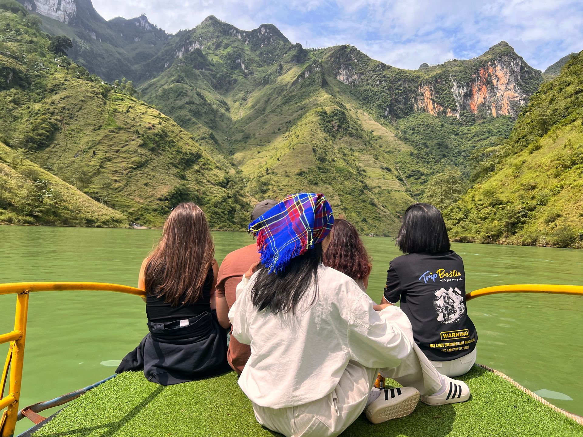 Travelers on a boat tour on the Nho Que River. One wears a TripBestie t-shirt.