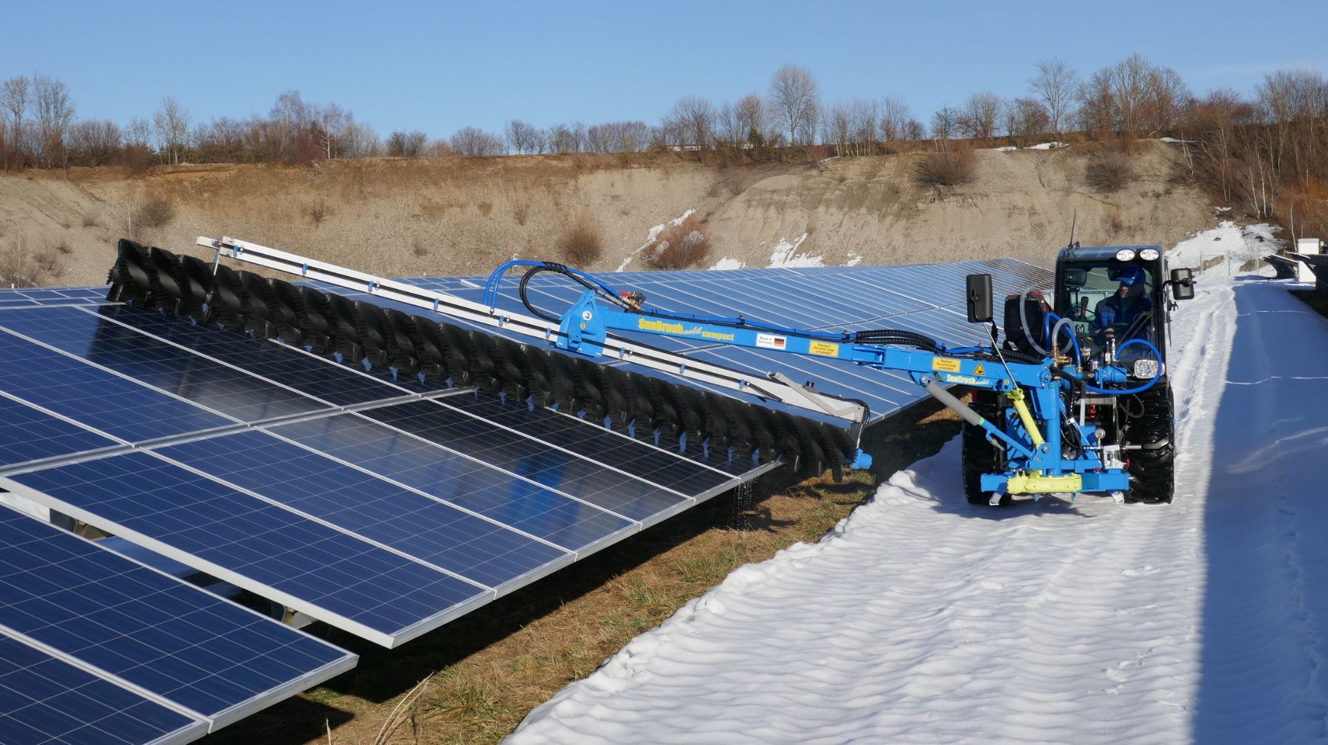 a blue tractor is cleaning solar panels in the snow