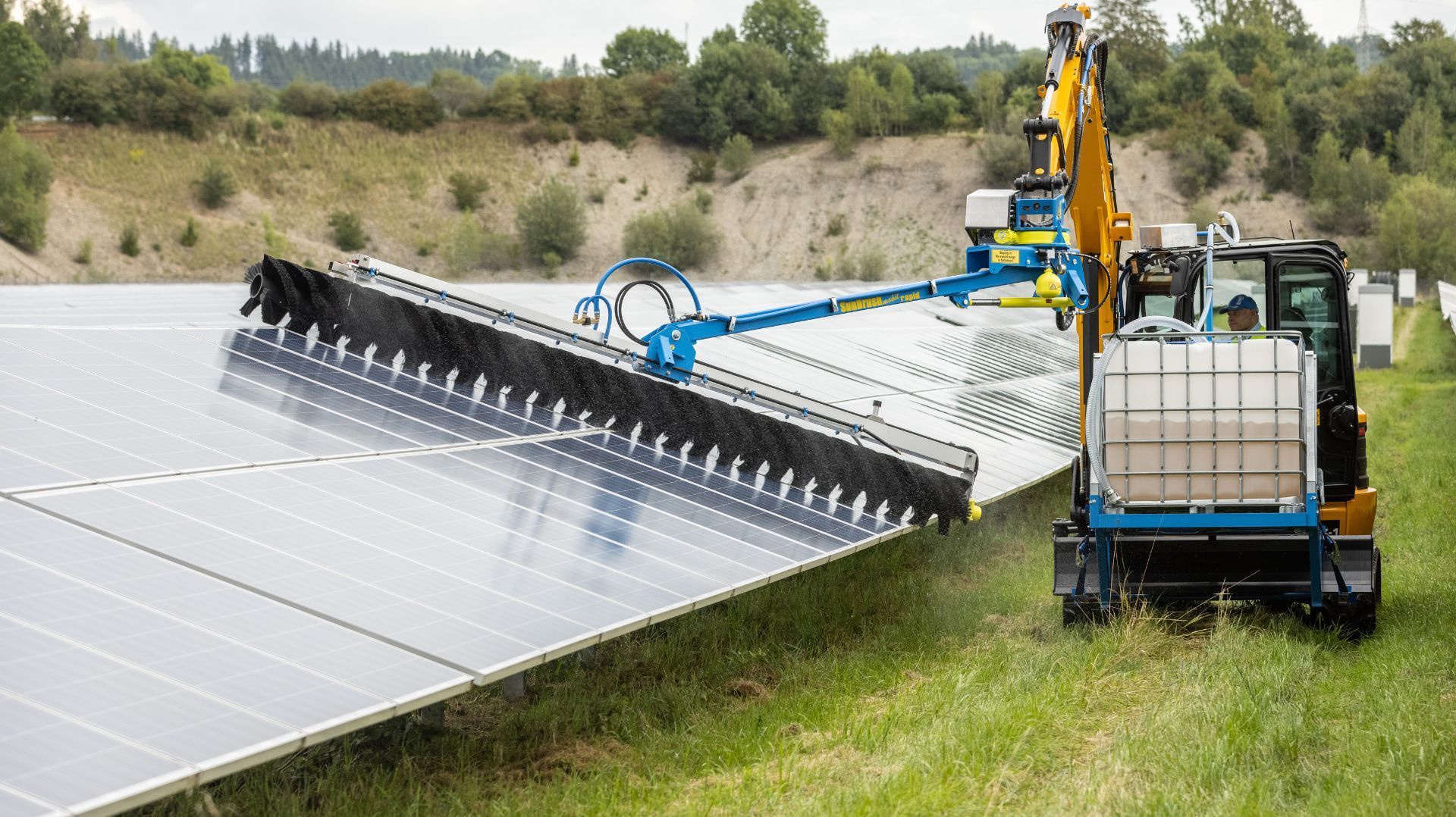 a blue and yellow excavator is cleaning solar panels in a field .