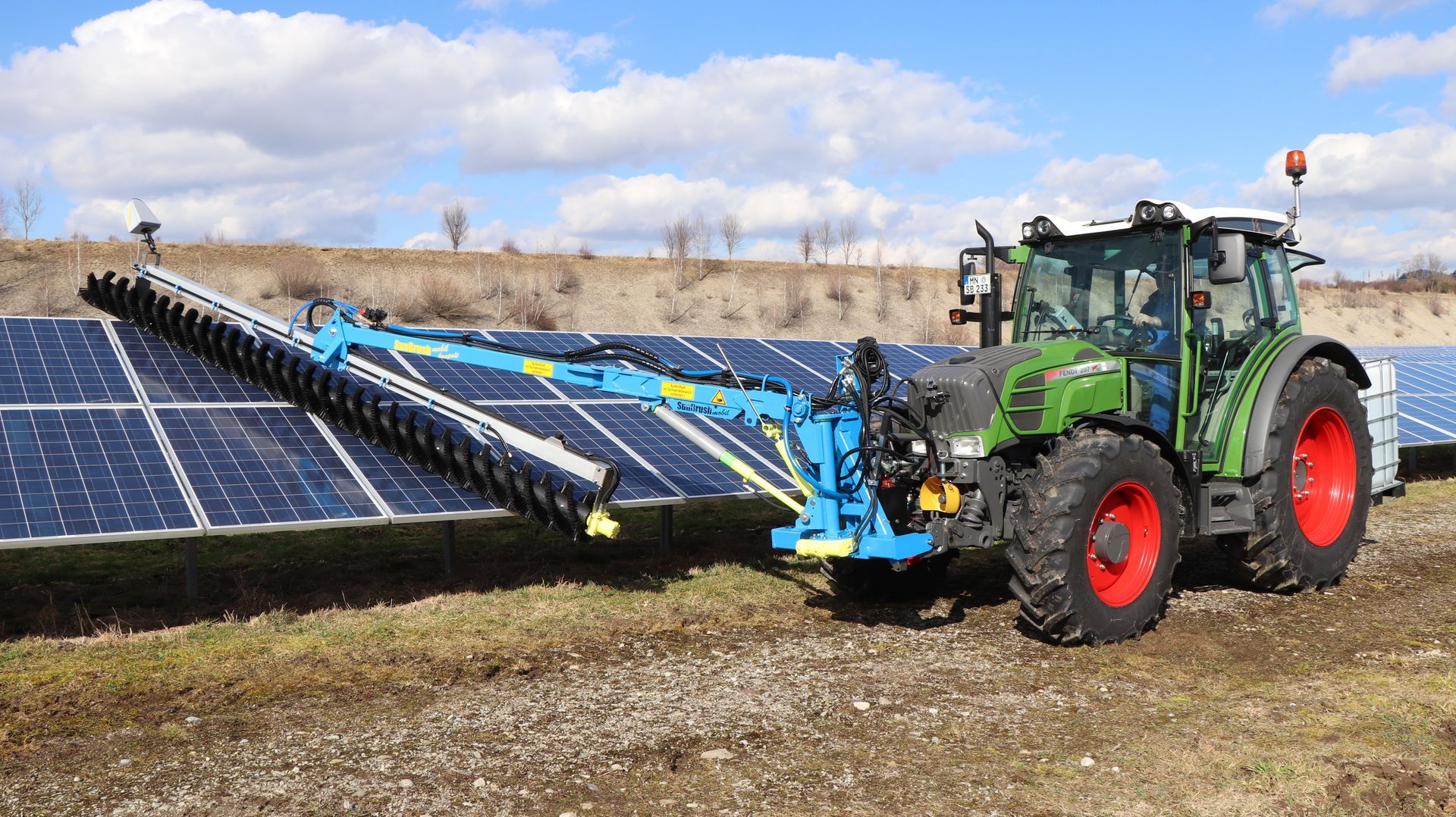 a green tractor is cleaning solar panels in a field .
