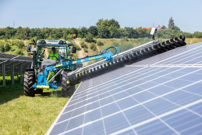 a green tractor is cleaning solar panels in a field .