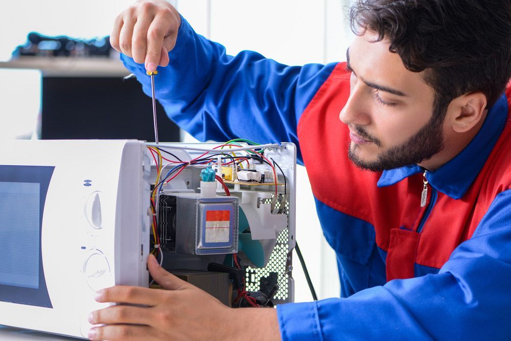 A Man is Fixing a Microwave With a Screwdriver — Commercial Kitchens Direct in Southern Highlands, NSW