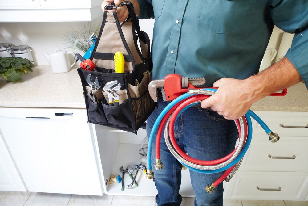 A Plumber is Holding a Hose and a Tool Bag — Commercial Kitchens Direct in Shoalhaven, NSW