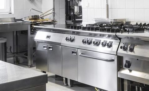 A Woman Wearing Purple Gloves is Cleaning an Oven in a Kitchen — Commercial Kitchens Direct in Southern Highlands, NSW