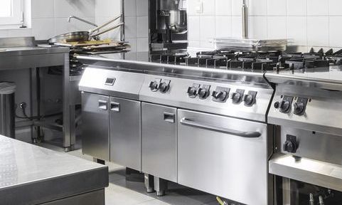 A Woman Wearing Purple Gloves is Cleaning an Oven in a Kitchen — Commercial Kitchens Direct in Unanderra, NSW