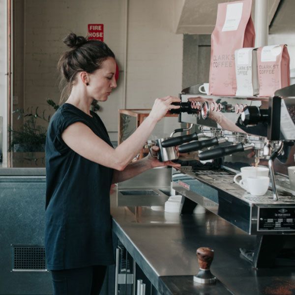 A Woman in a Black Shirt is Pouring Coffee Into a Cup — Commercial Kitchens Direct in Unanderra, NSW