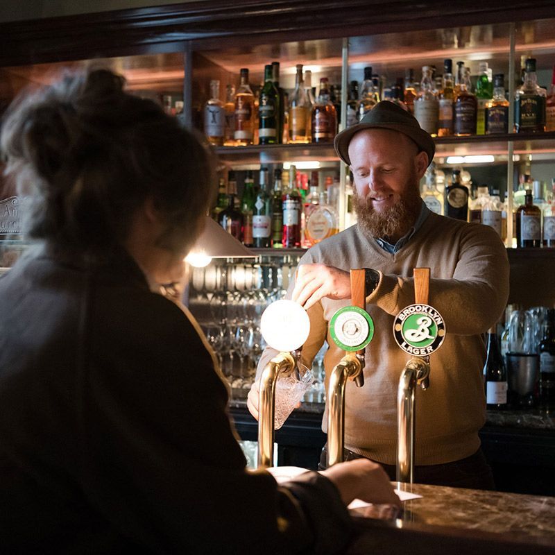 A Man in a Hat is Pouring Beer Into a Glass — Commercial Kitchens Direct in Unanderra, NSW