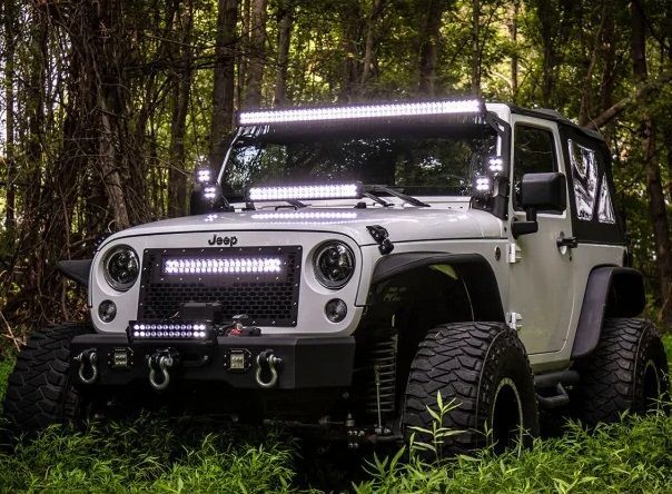 A white jeep with a light bar on top of it is parked in the woods.