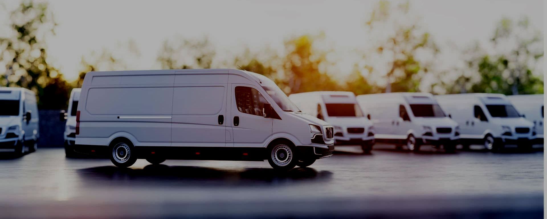 A row of white commercial vans are parked in a parking lot.