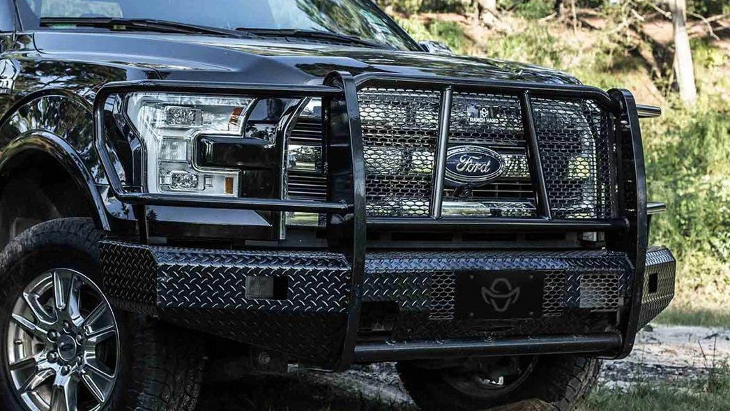 A black truck with a grill on the front is parked in the grass.