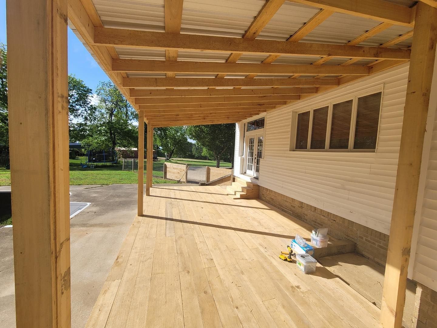 A wooden deck is sitting under a wooden roof next to a house.
