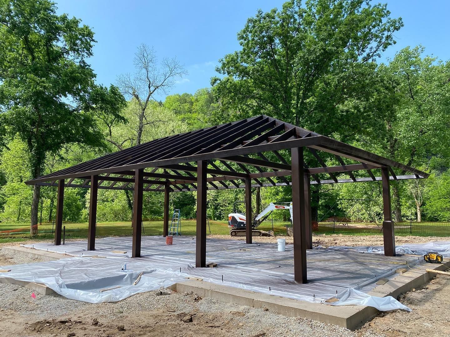 A wooden structure is being built in a park with trees in the background.