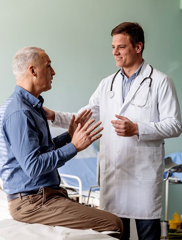 Doctor in white coat comforts patient sitting on exam table, both smiling.