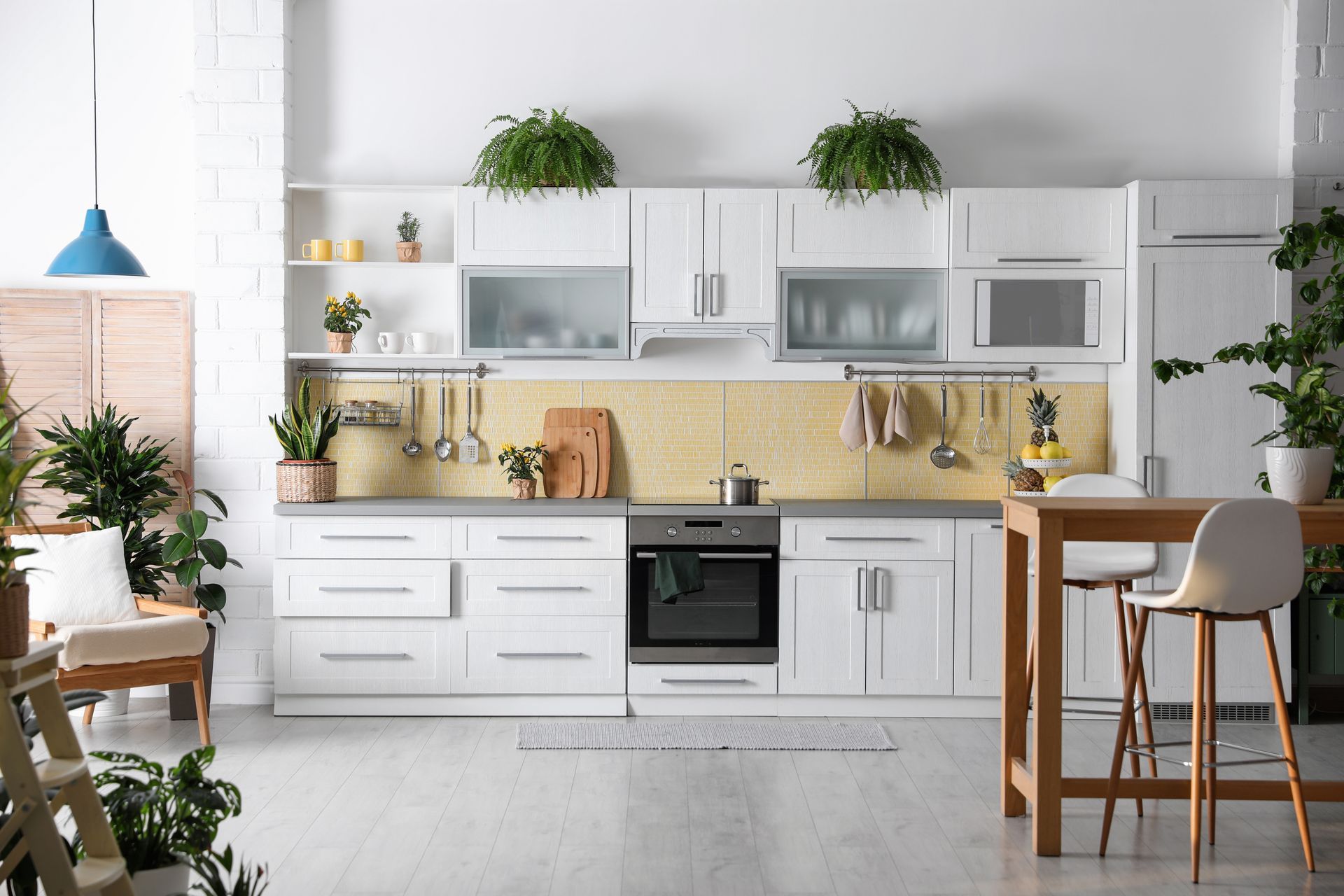 A kitchen with white cabinets , a table , chairs , and plants.
