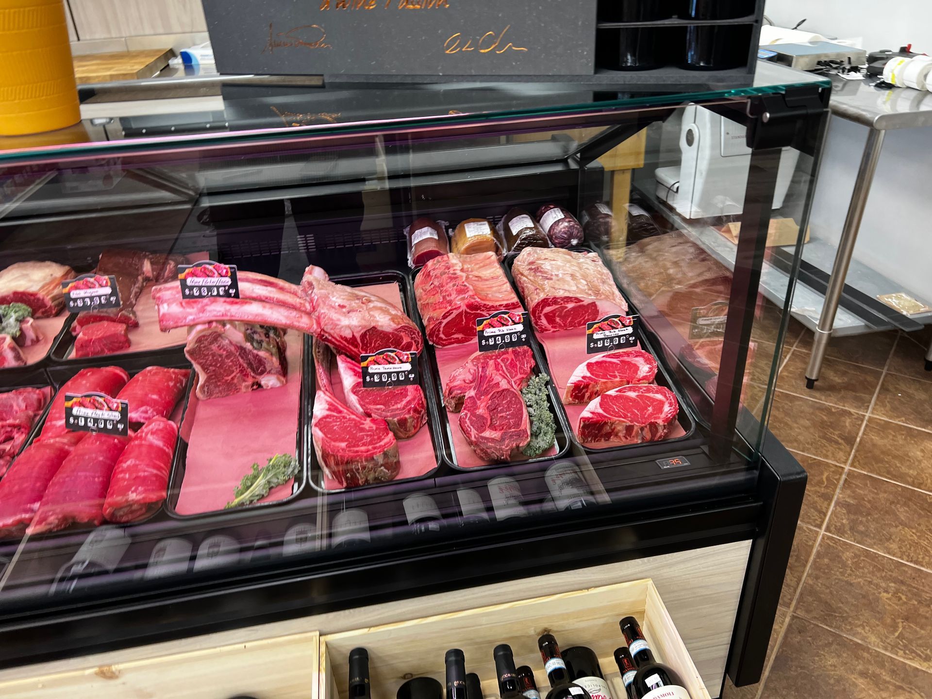 A butcher 's display case filled with meat and wine bottles.