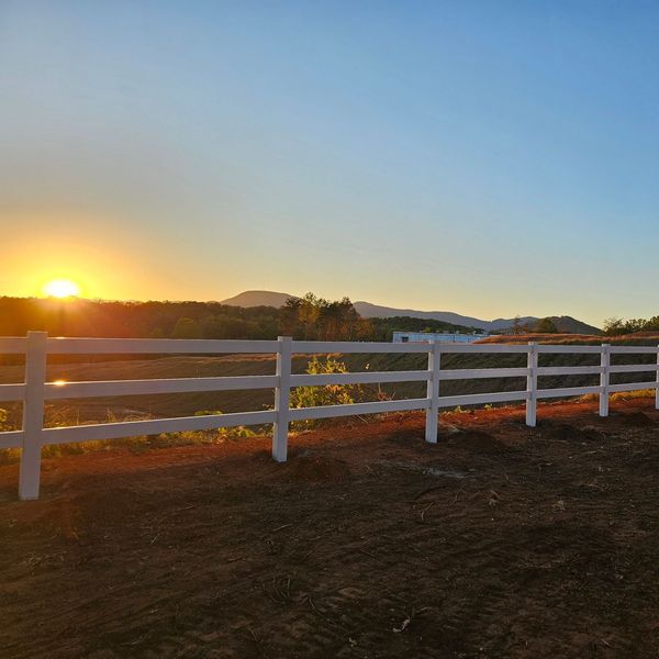 A white fence surrounds a field with a sunset in the background.