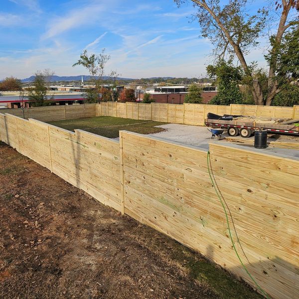 A long wooden fence surrounds a yard with a trailer in the background.