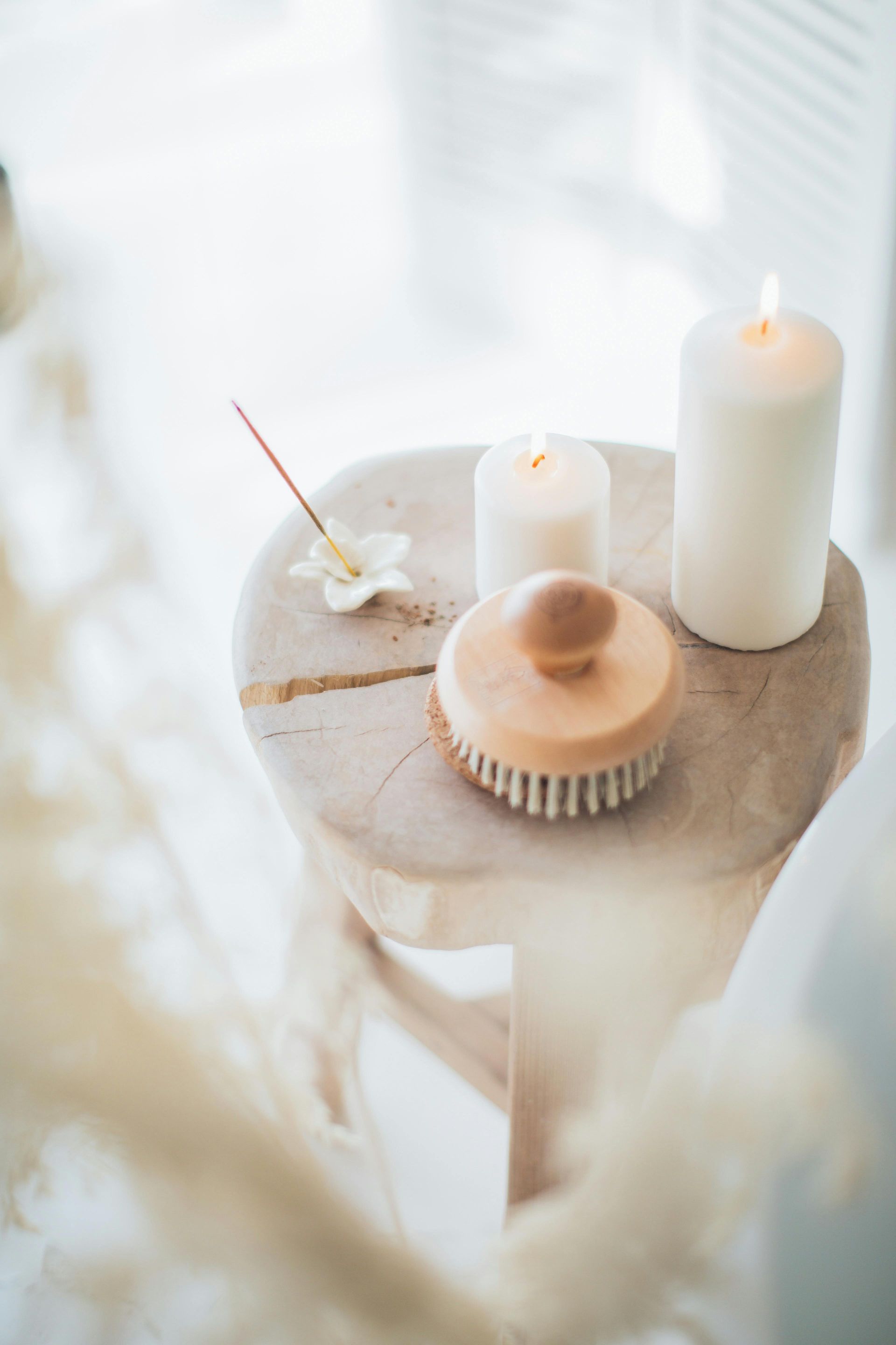A wooden stool holding lit candles, a dry brush, a flower, and incense, in a bright, minimalist space.