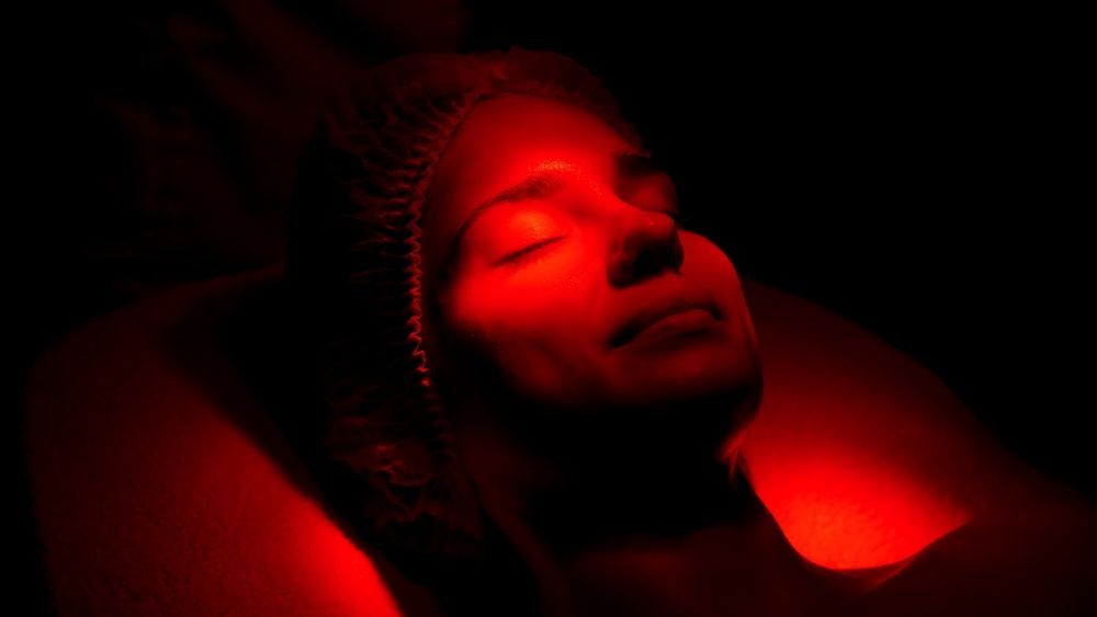 Woman reclining, face illuminated in red light, eyes closed, dark background.
