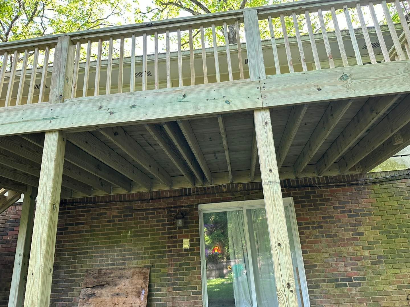 Wooden deck with railings above a brick wall, overlooking a sliding glass door.