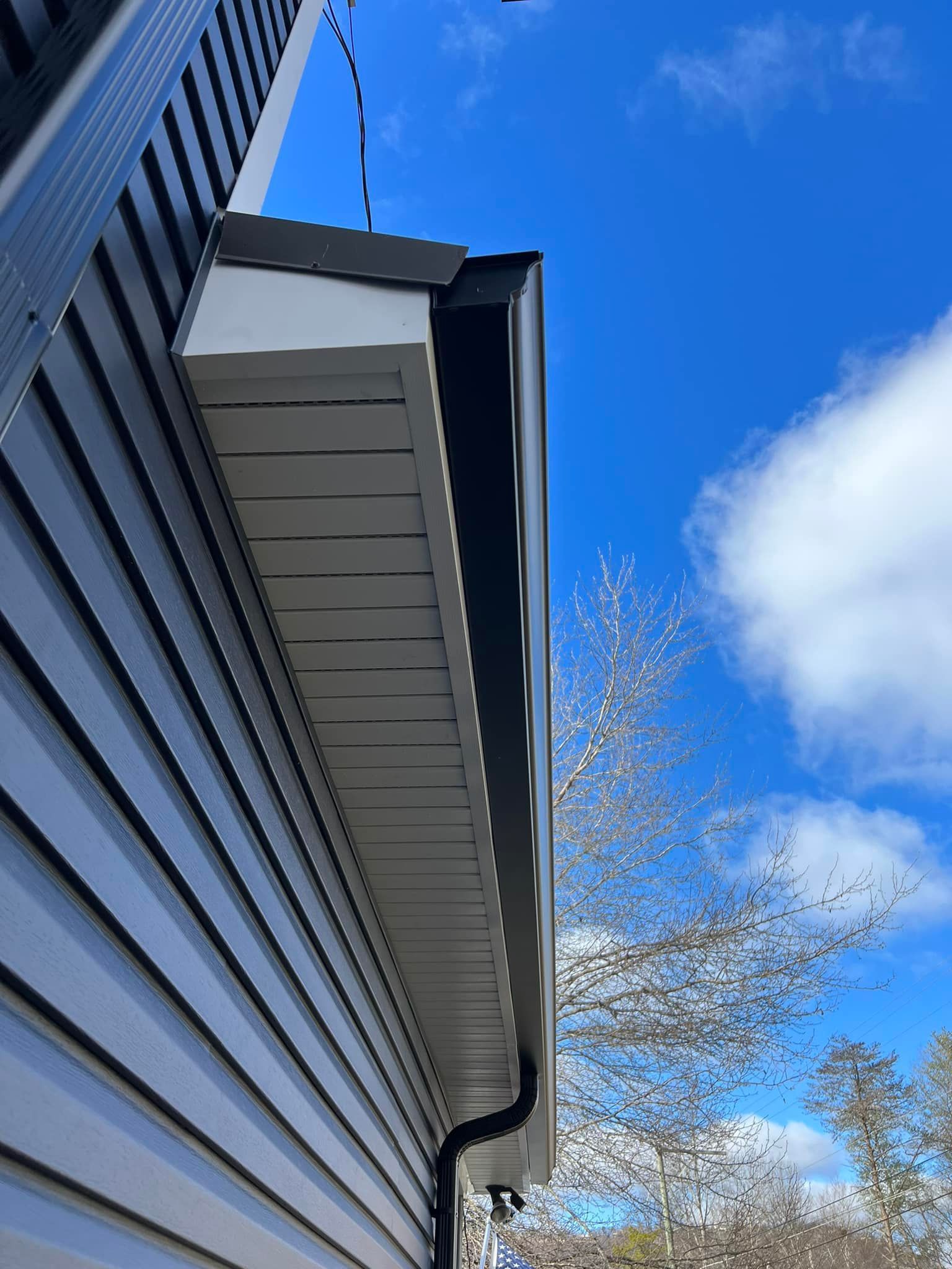 Black and gray house siding with white soffit, black gutter, and a bright blue sky.