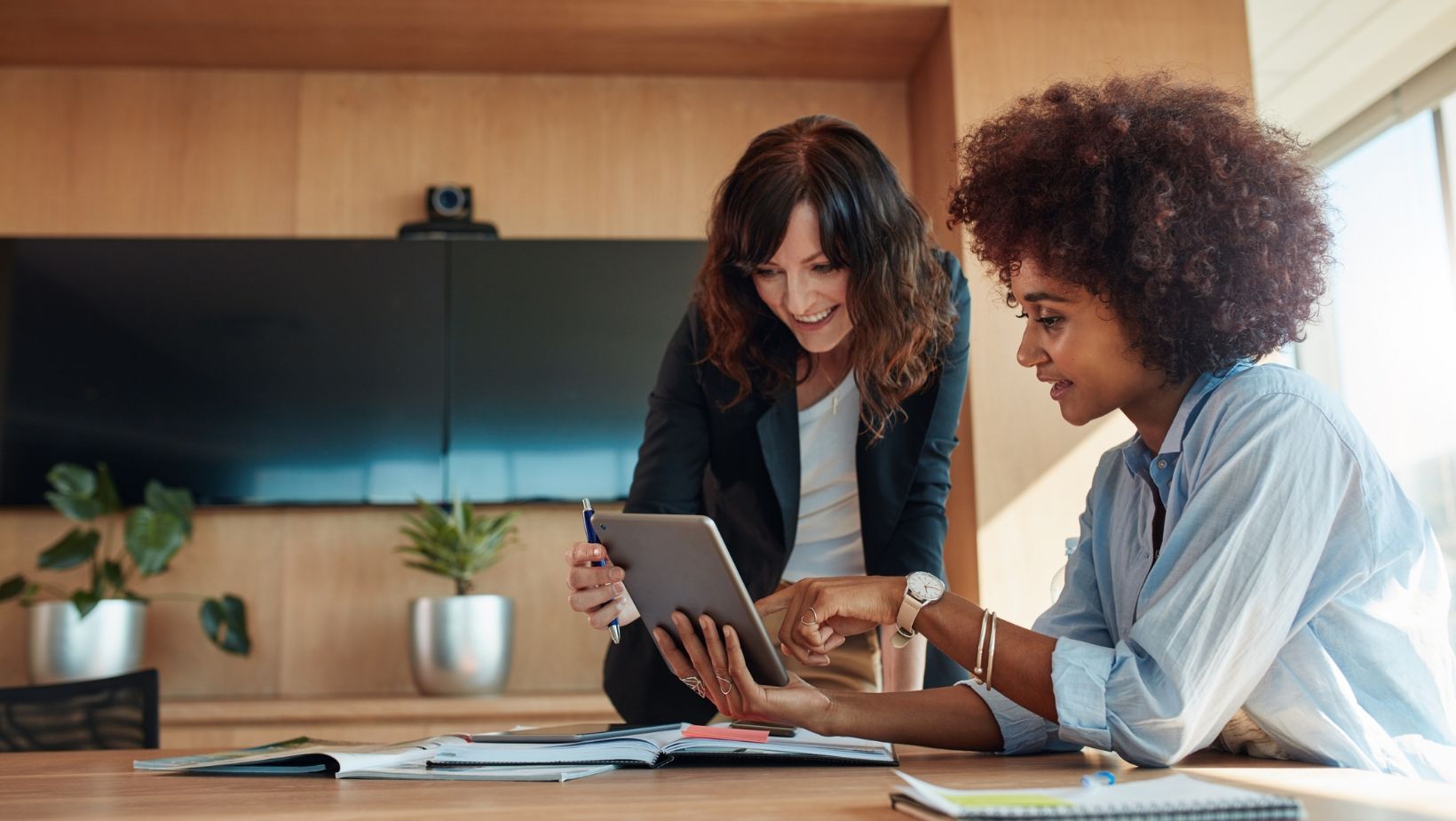 Two women are sitting at a table looking at a tablet.