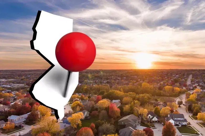 Red pin marking a white state outline over a sunset aerial view of a suburban neighborhood.