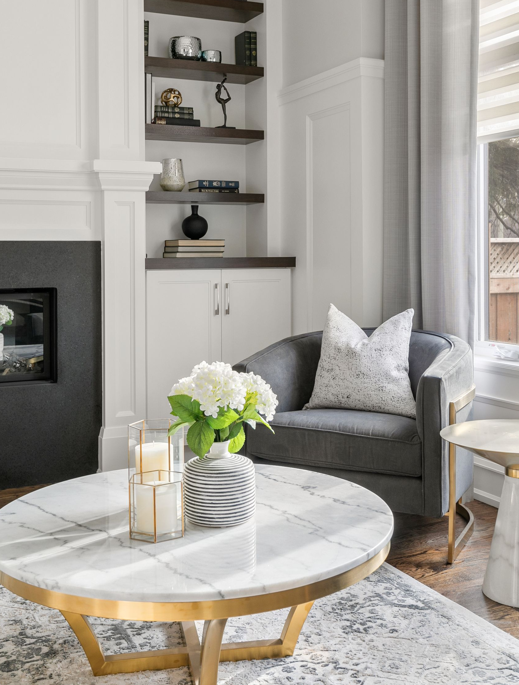 Cozy living room with gray armchair, marble coffee table, fireplace, and built-in shelves.