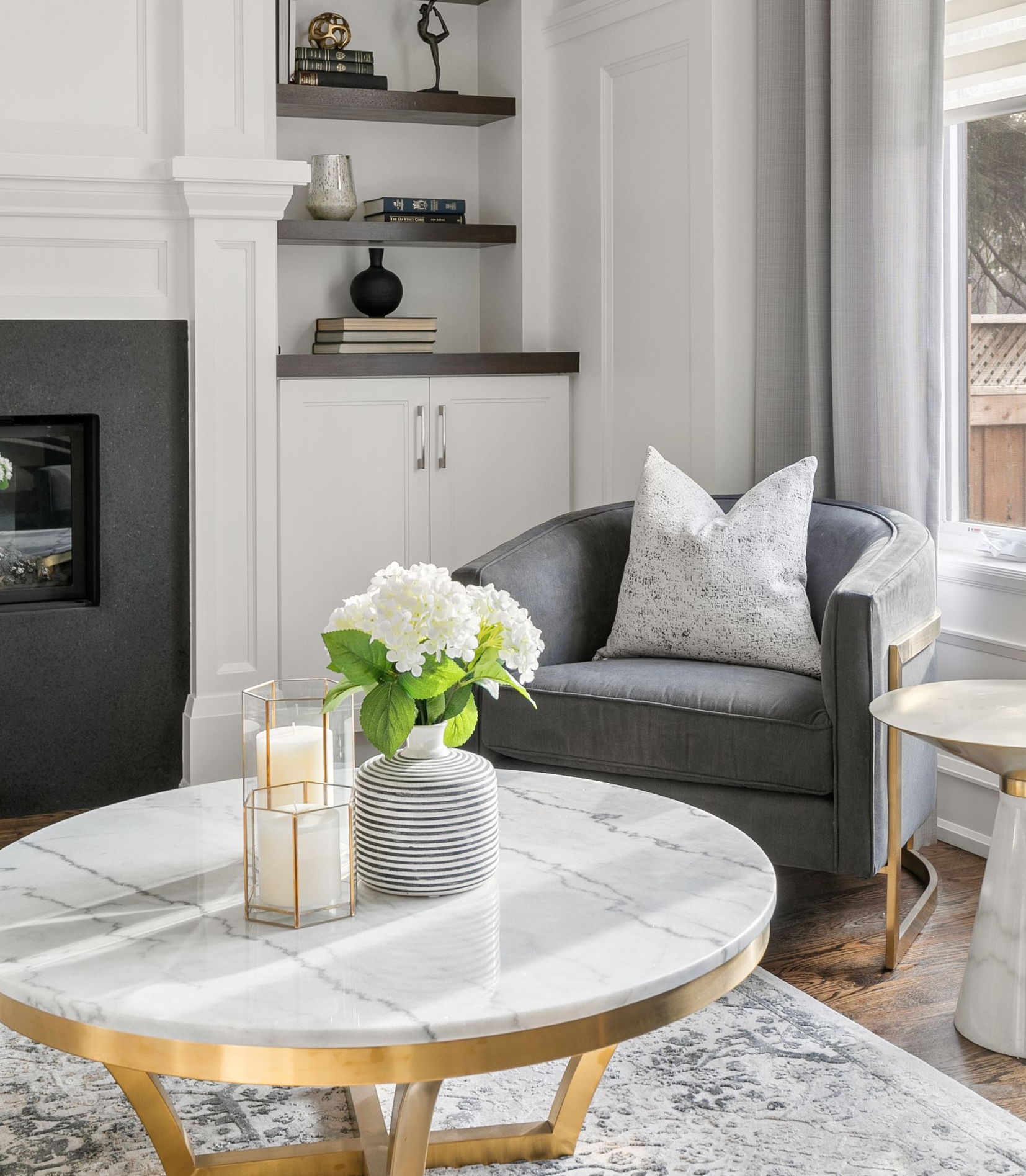 Living room: gray armchair, marble coffee table, built-in shelves with decor, and a white fireplace.