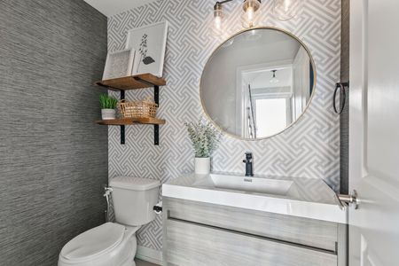 Small bathroom with patterned wallpaper, round mirror, floating shelves, and a white toilet.