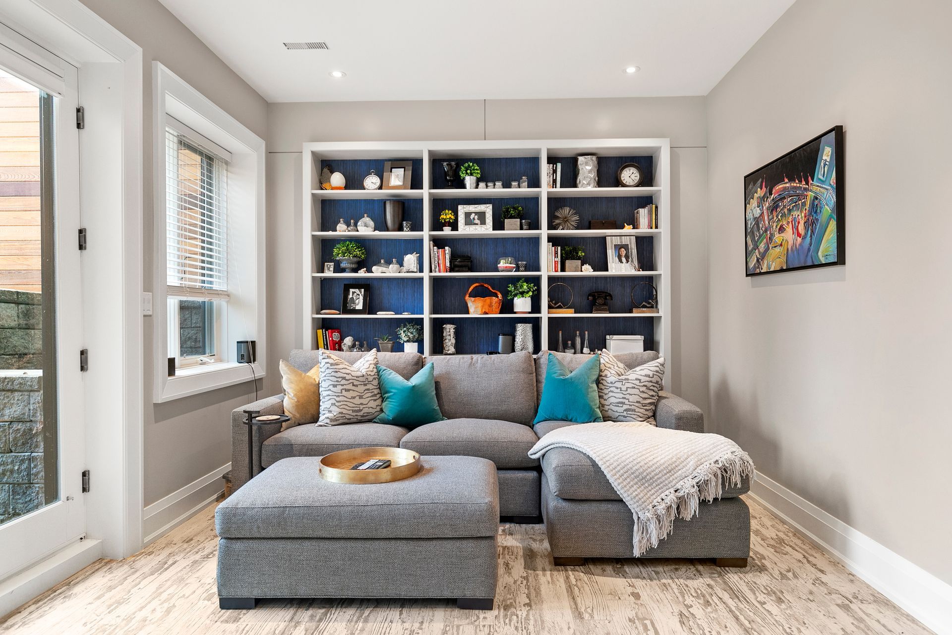 Cozy living room with gray sectional, ottoman, and built-in bookshelves filled with decor.