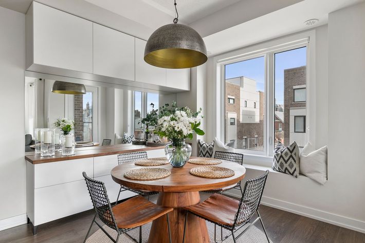 Dining room with round wooden table, four chairs, and window seat. White cabinets and a decorative pendant light.