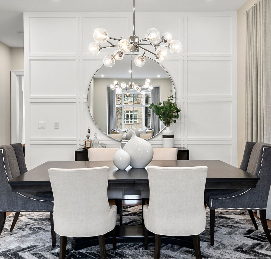 Formal dining room with white walls, dark table, light chairs, and a large mirror.