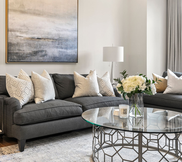 Living room with gray couch, glass coffee table, and abstract art.