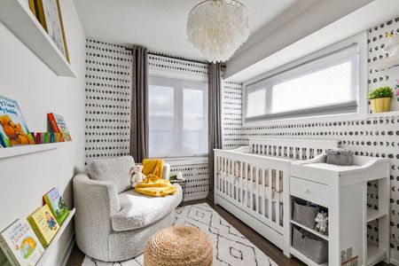 A nursery with white furniture, patterned wallpaper, and a cozy armchair.