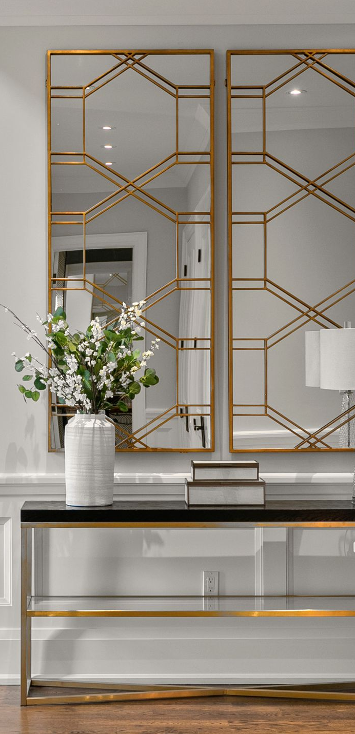 Gold framed geometric mirrors, a console table with decor, and a flower arrangement in a vase.