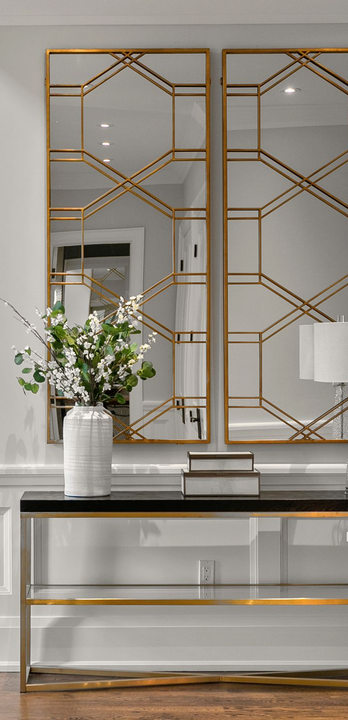 Gold framed geometric mirrors, a console table with decor, and a flower arrangement in a vase.
