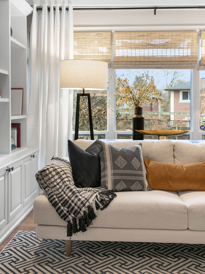 Living room with white couch, patterned pillows and rug, window, and a floor lamp.