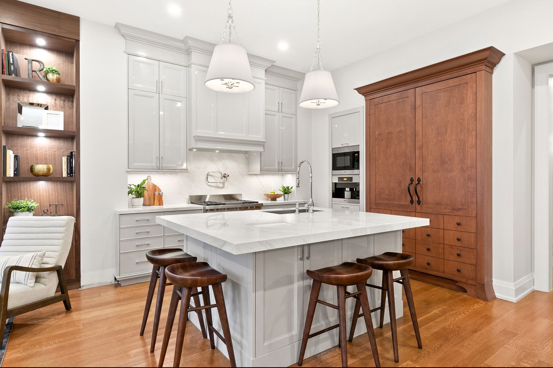 Modern kitchen with island, stools, cabinetry, and built-in appliances. Hardwood floors and white countertops.