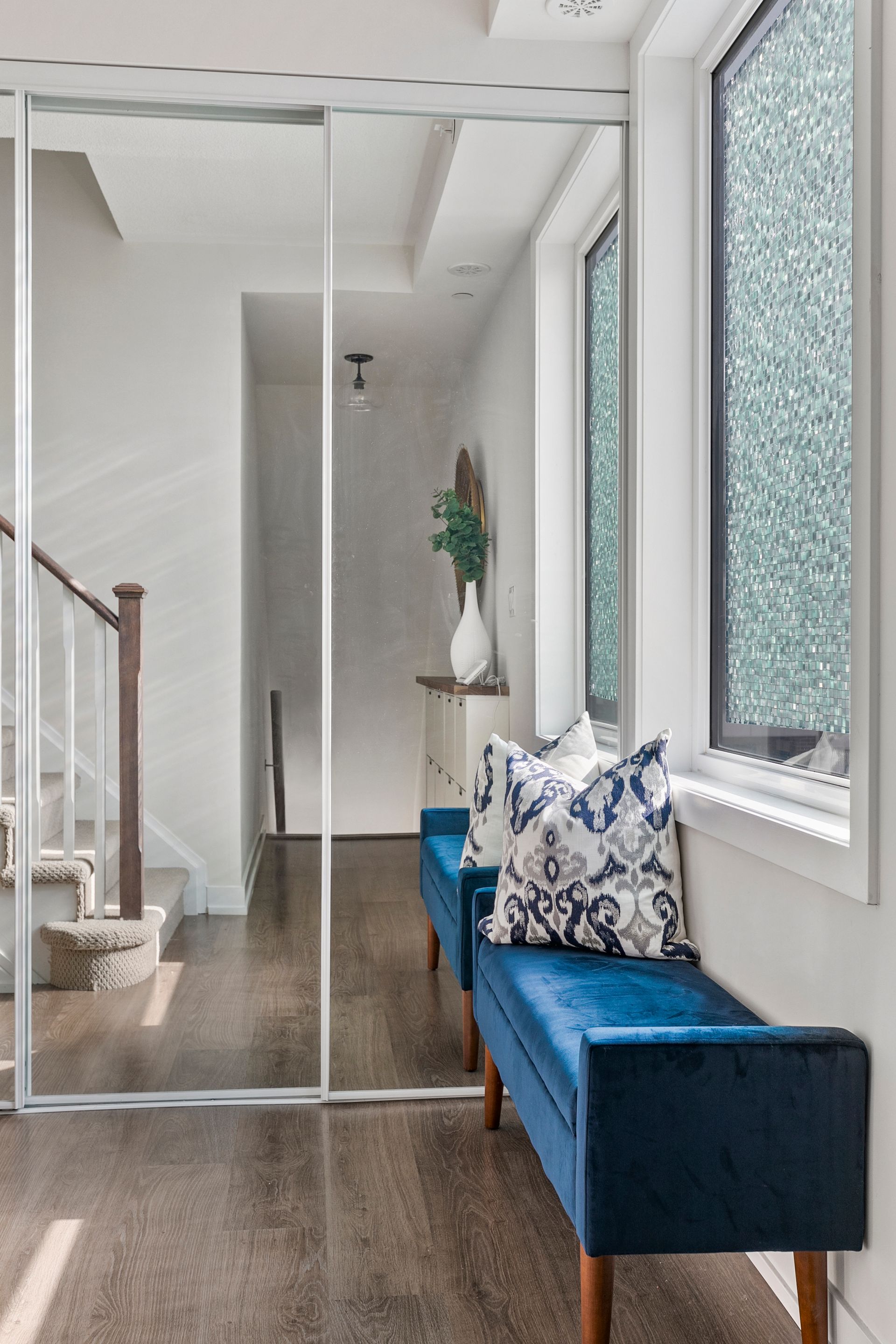 Hallway with dark wood floor, two blue velvet benches with pillows, and a large mirror.