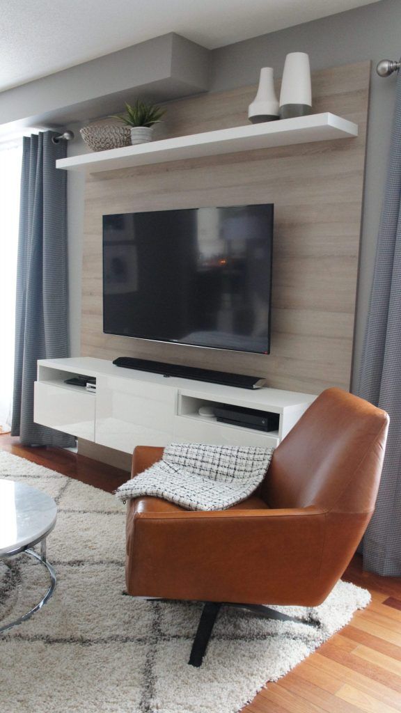 Living room with a TV, floating shelves, brown leather chair, and gray curtains.