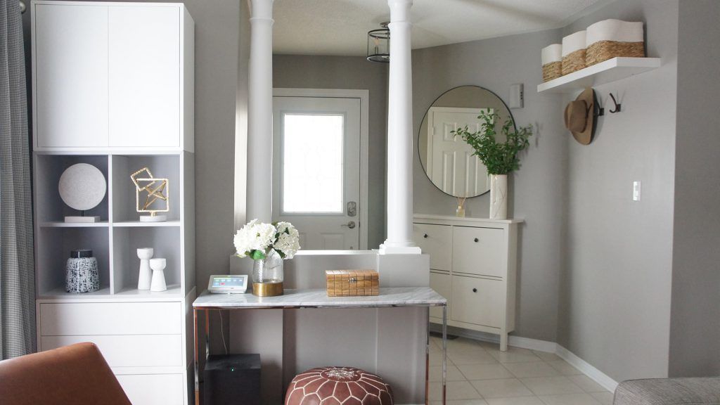 Modern entryway with white storage, columns, desk, and decorative items. Gray walls and a round mirror.