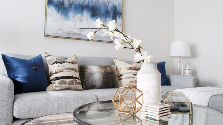 Living room with gray sofa, blue and patterned pillows, abstract art, and decor on a round coffee table.