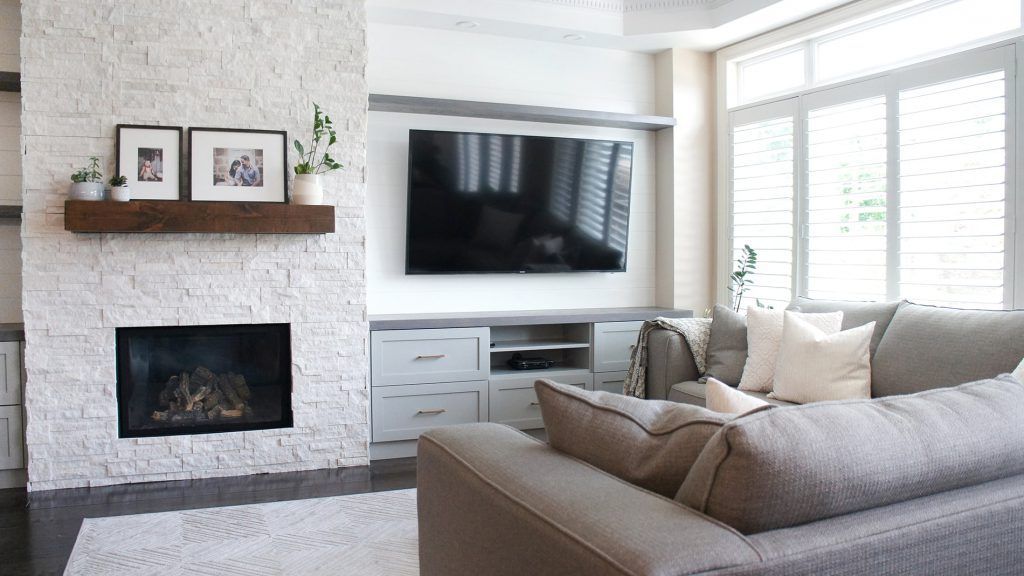 Living room with fireplace, TV, and gray sectional sofa. White brick fireplace with wooden mantel.
