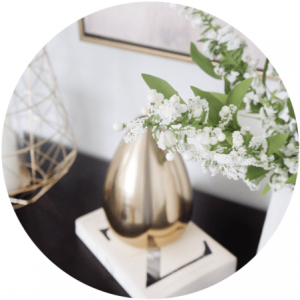 Gold vase with white flowers on a book, beside a gold geometric object.