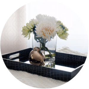 Black tray with flowers in a vase and a gold bird figurine on a white surface.