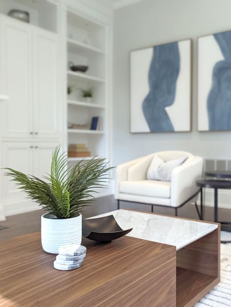 Living room with white built-in shelving, cream armchair, abstract blue art, and wooden coffee table with a plant.